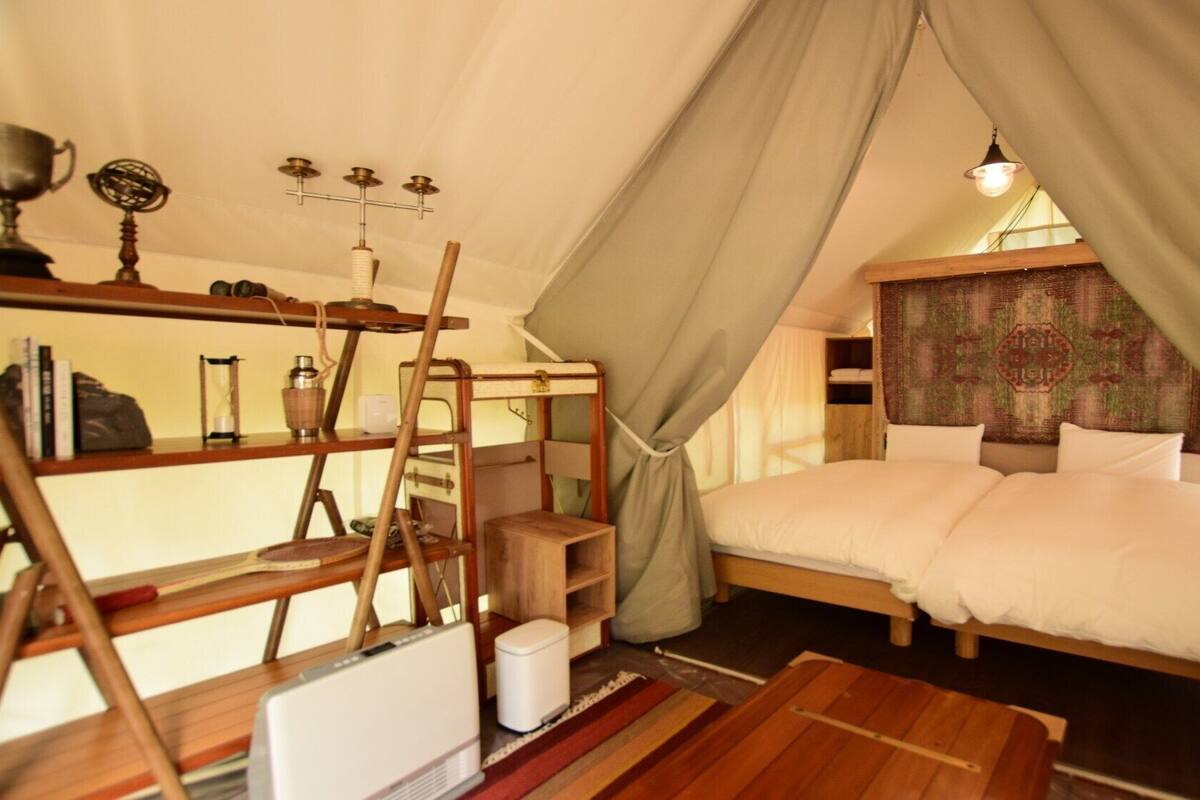 A cozy tent-style room with a bed, shelves with books and decorative items, a small table, and a hanging light fixture.