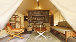 A cozy tent with a wooden table, a cushioned chair, a sofa, and a shelf with decorative items. - Glamorous Dining Tateshina The Camp (Chino)