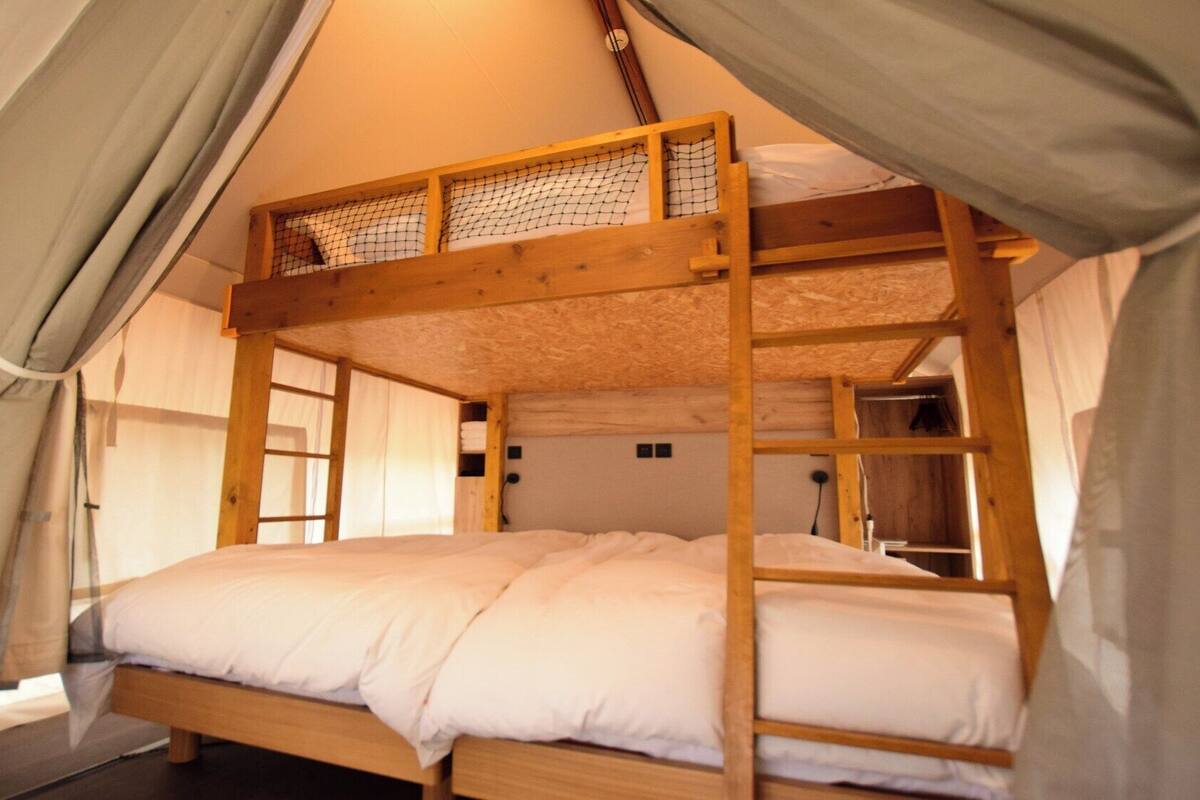 A bunk bed in a tent-like structure with a netted upper bunk and a lower bunk.