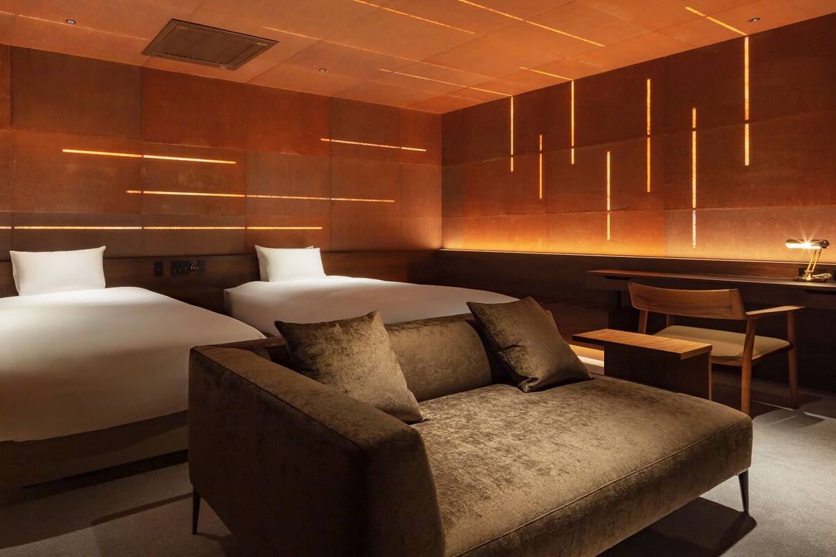 A hotel room with two beds, a sofa, a desk, and a chair.