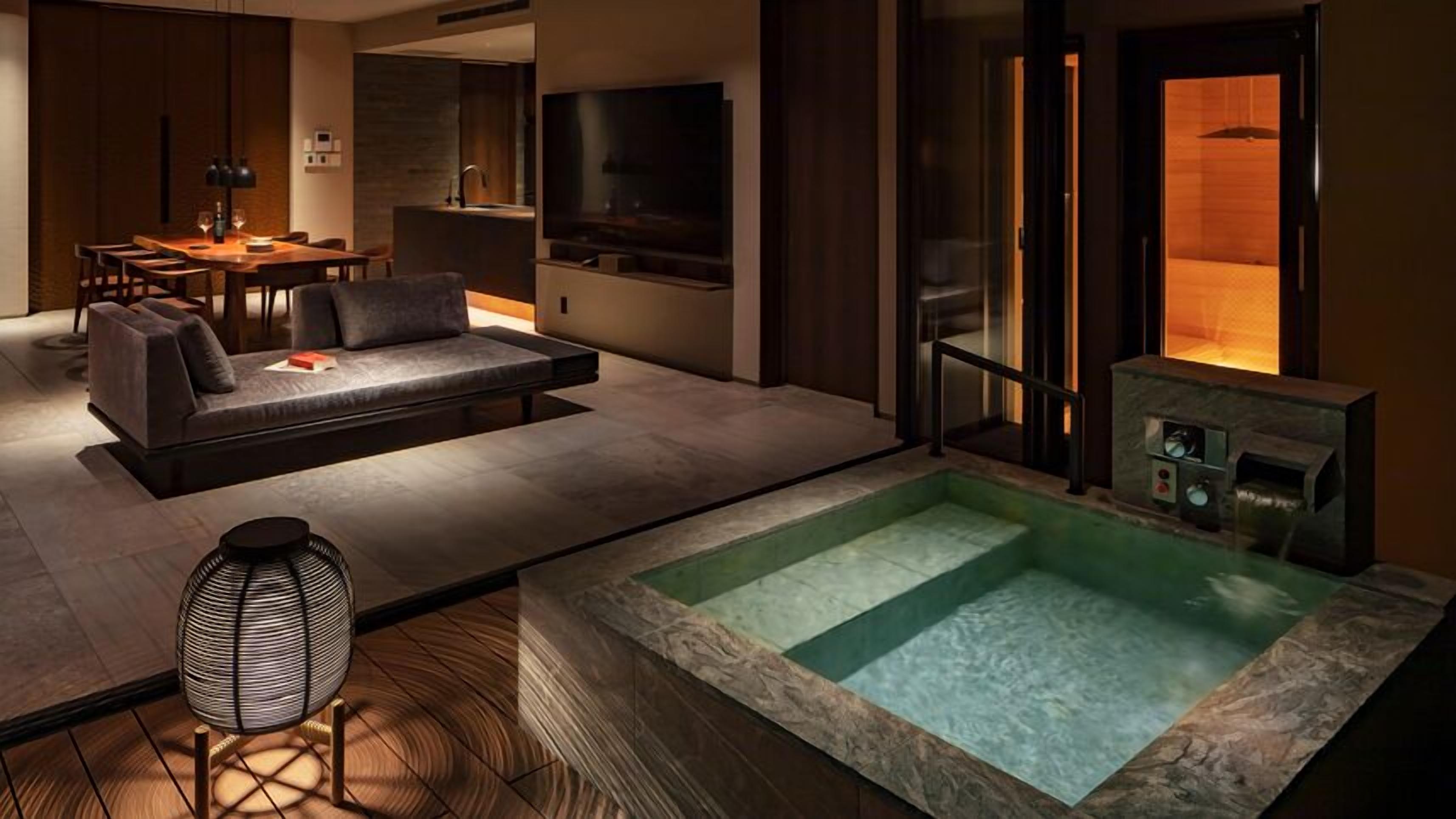 A modern living room with a sofa, a dining table, and a TV. There is a hot tub in the center.
