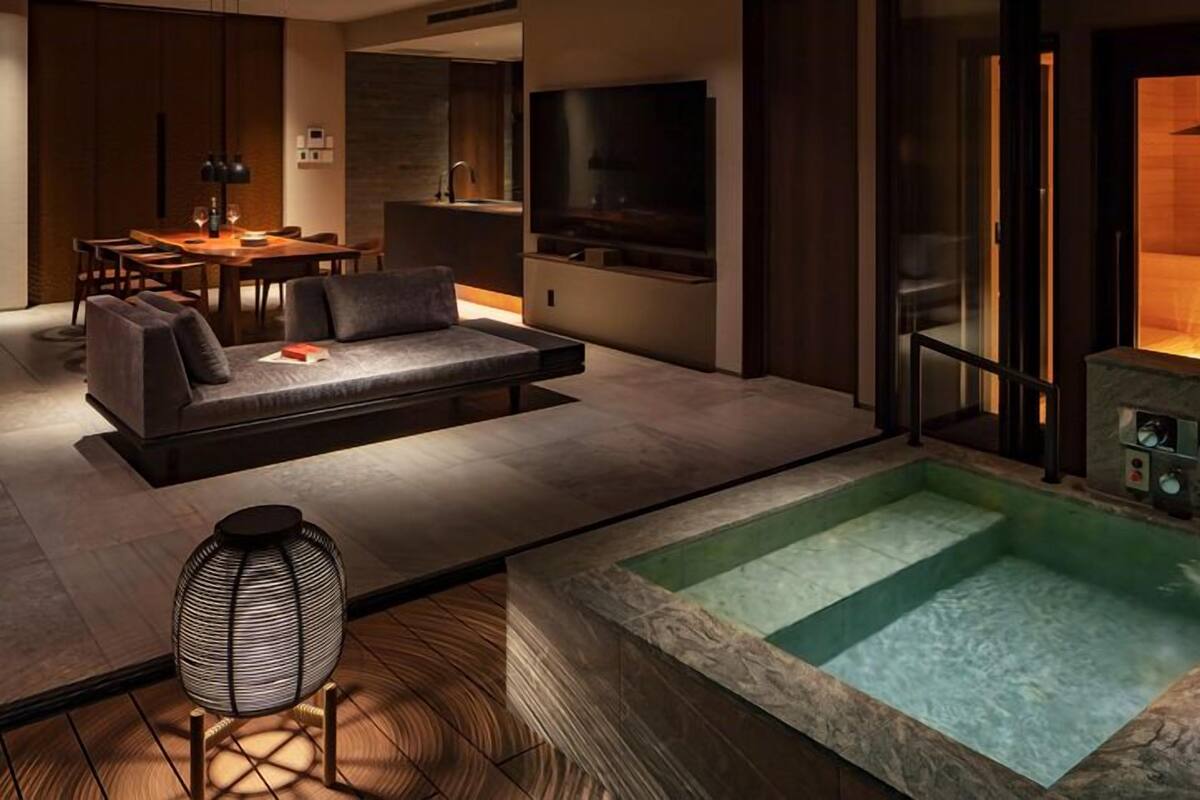 A modern living room with a sofa, a dining table, and a TV. There is a hot tub in the center.