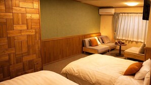 Hotellihuone, jossa on kaksi sänkyä, sohva, pieni pöytä teekannuineen ja ikkuna, jossa on verhot.