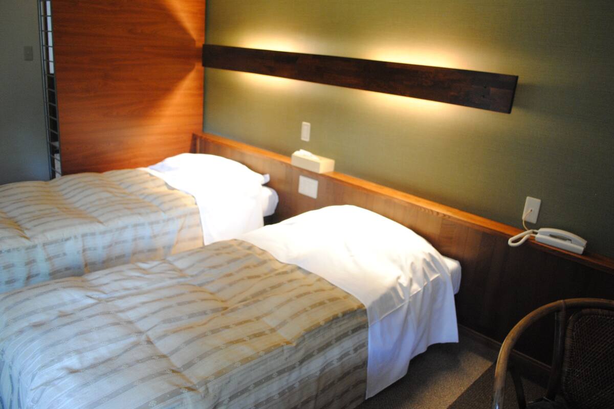 Una habitación de hotel con dos camas, cabecero de madera, teléfono en la mesita de noche y una silla.