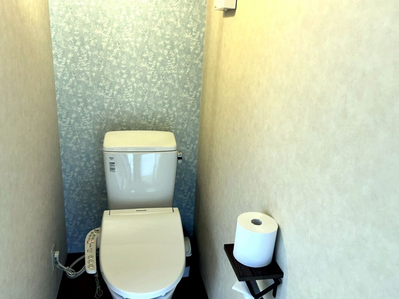 Et lille badeværelse med toilet, papirhåndklædeholder og en væg med blomstermønster.
