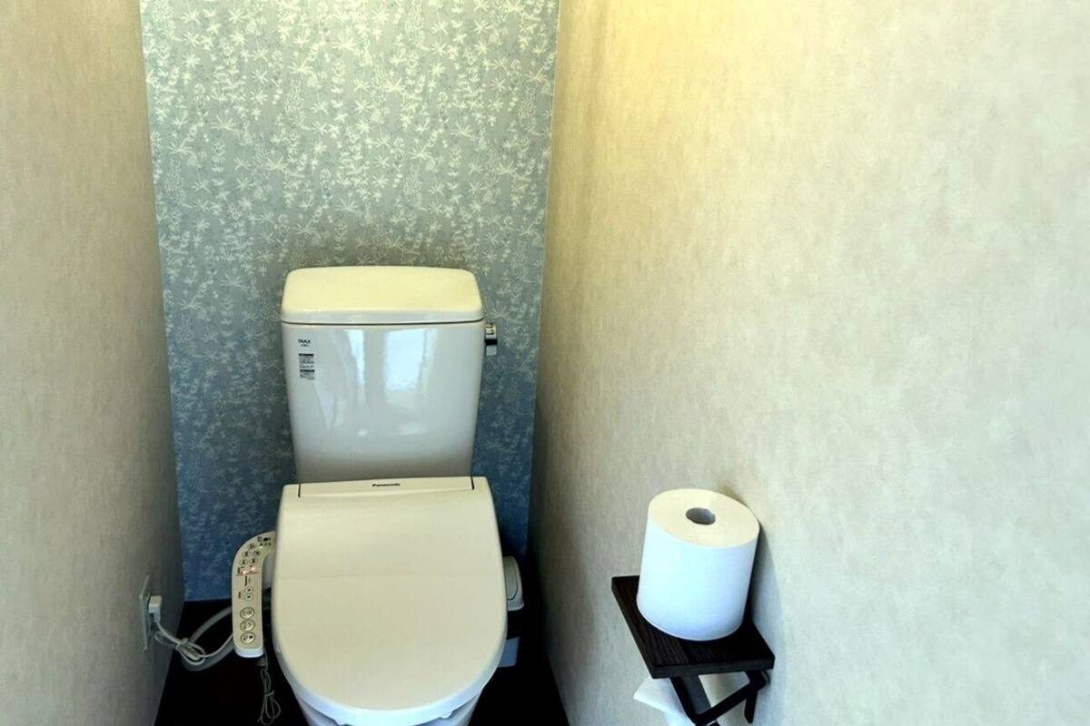 Un baño pequeño con inodoro, un dispensador de toallas de papel y una pared con estampado floral.
