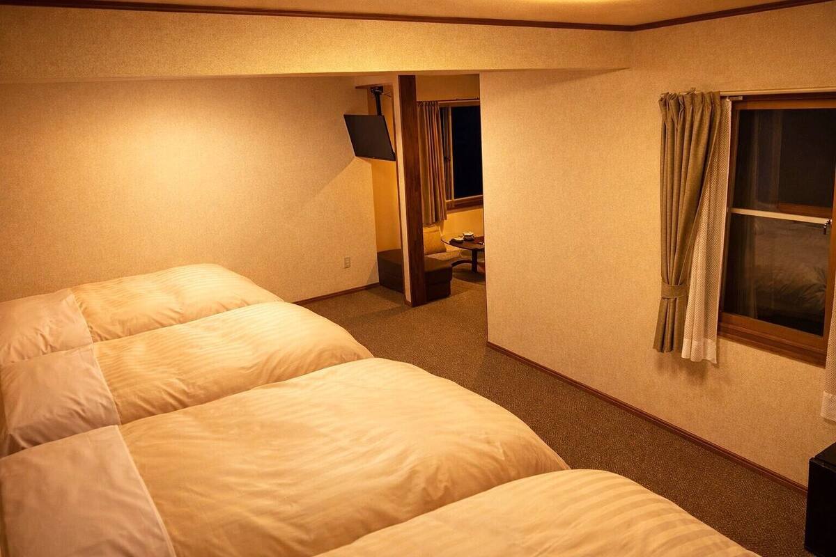 Una habitación de hotel con dos camas, televisión, ventana con cortinas y una pequeña mesa con silla.