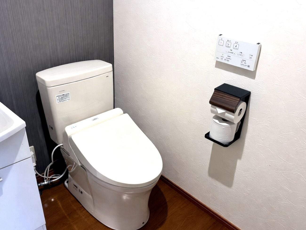 Et hvidt toilet med kontrolpanel og toiletpapirholder monteret på væggen.