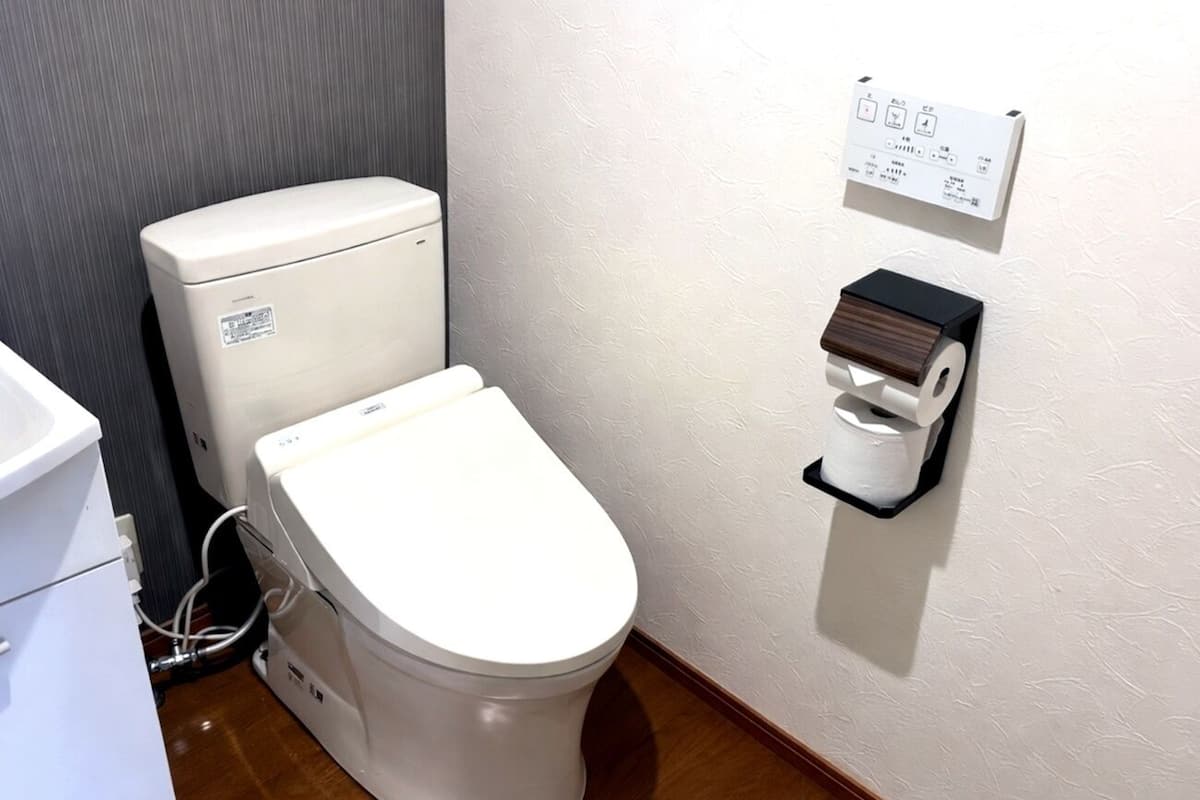 Des toilettes blanches dotées d’un panneau de commande et d’un porte-rouleau de papier toilette fixé au mur.