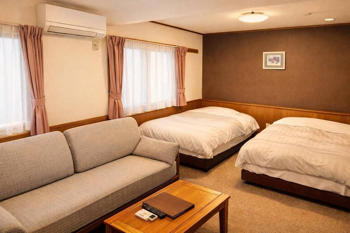 Una habitación de hotel con sofá, dos camas individuales, una mesa de madera y un equipo de aire acondicionado.