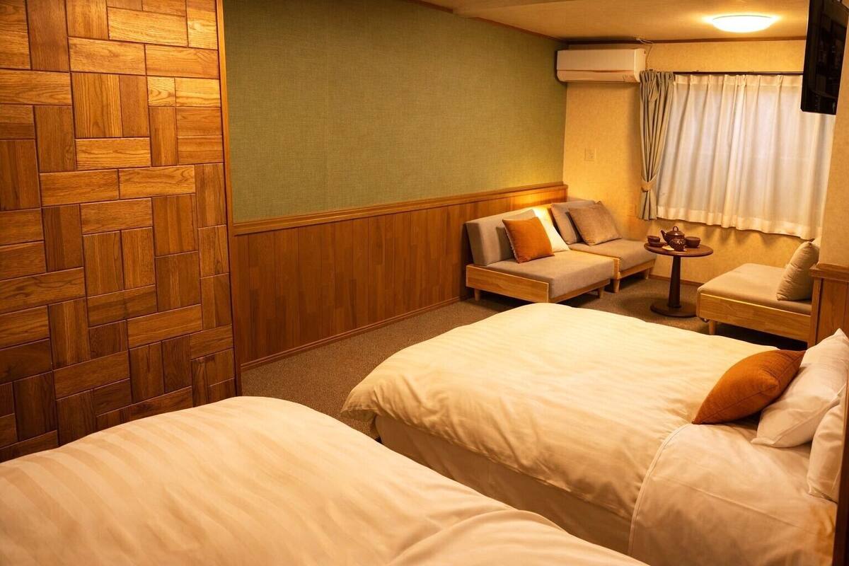 Una habitación de hotel con dos camas, un sofá, una mesita con tetera y un equipo de aire acondicionado.