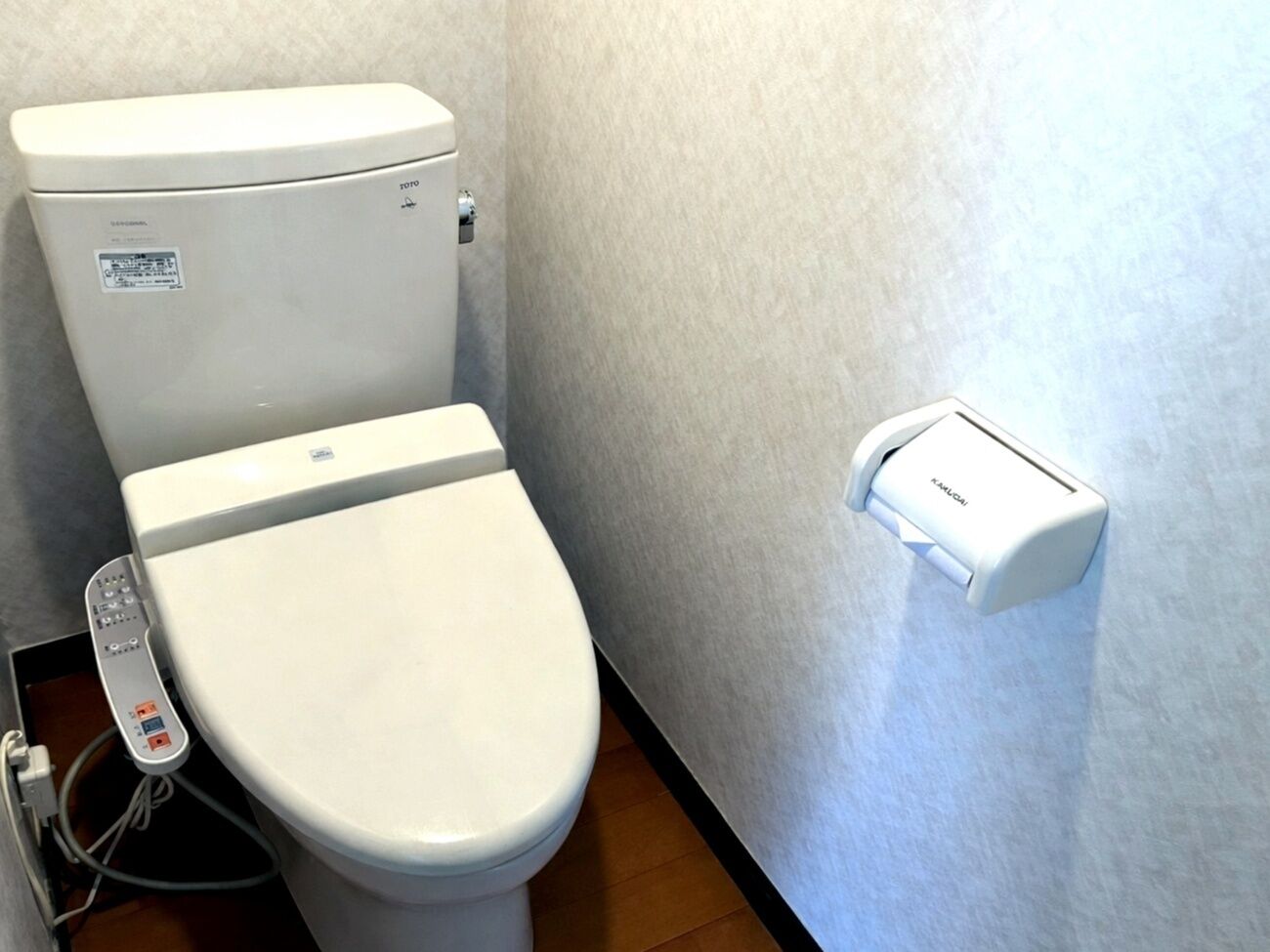 Toilet med kontrolpanel, vægmonteret bidet og en kontrolenhed på gulvet.