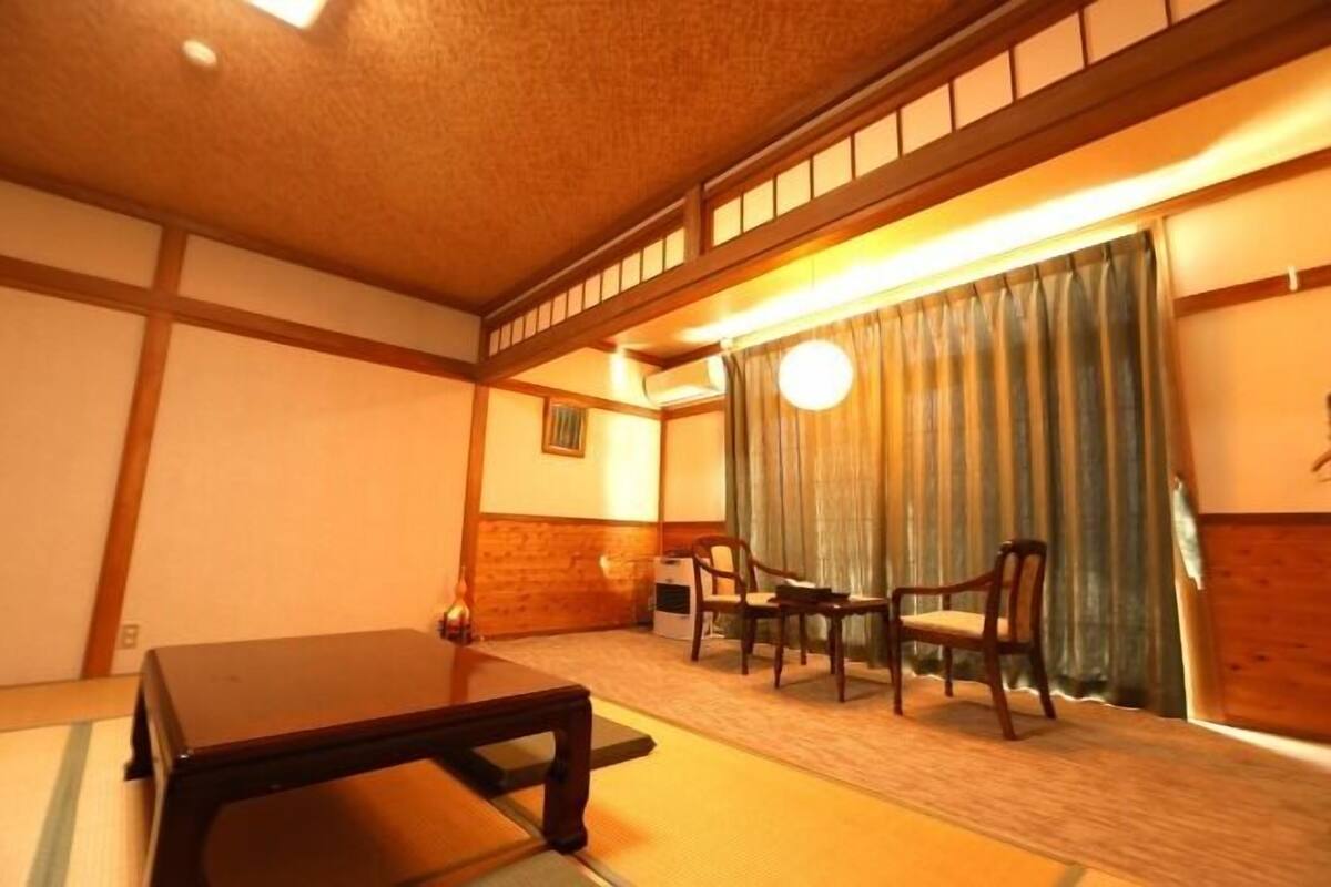 Una habitación japonesa tradicional con suelo de tatami, una mesa baja, dos sillas y un puertas correderas con cortinas.
