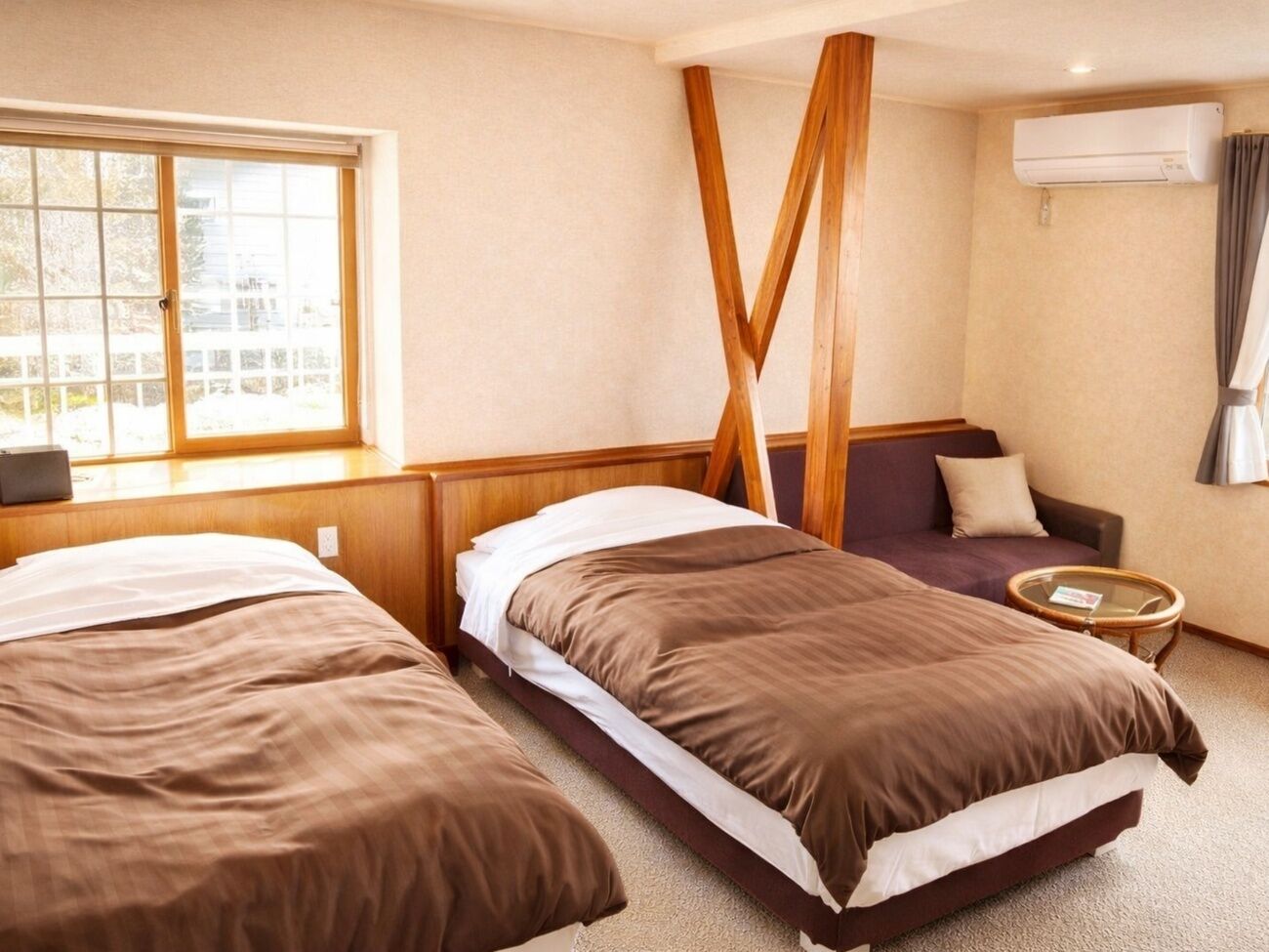 Habitación de hotel con dos camas, un sofá, una mesita redonda y un aire acondicionado.