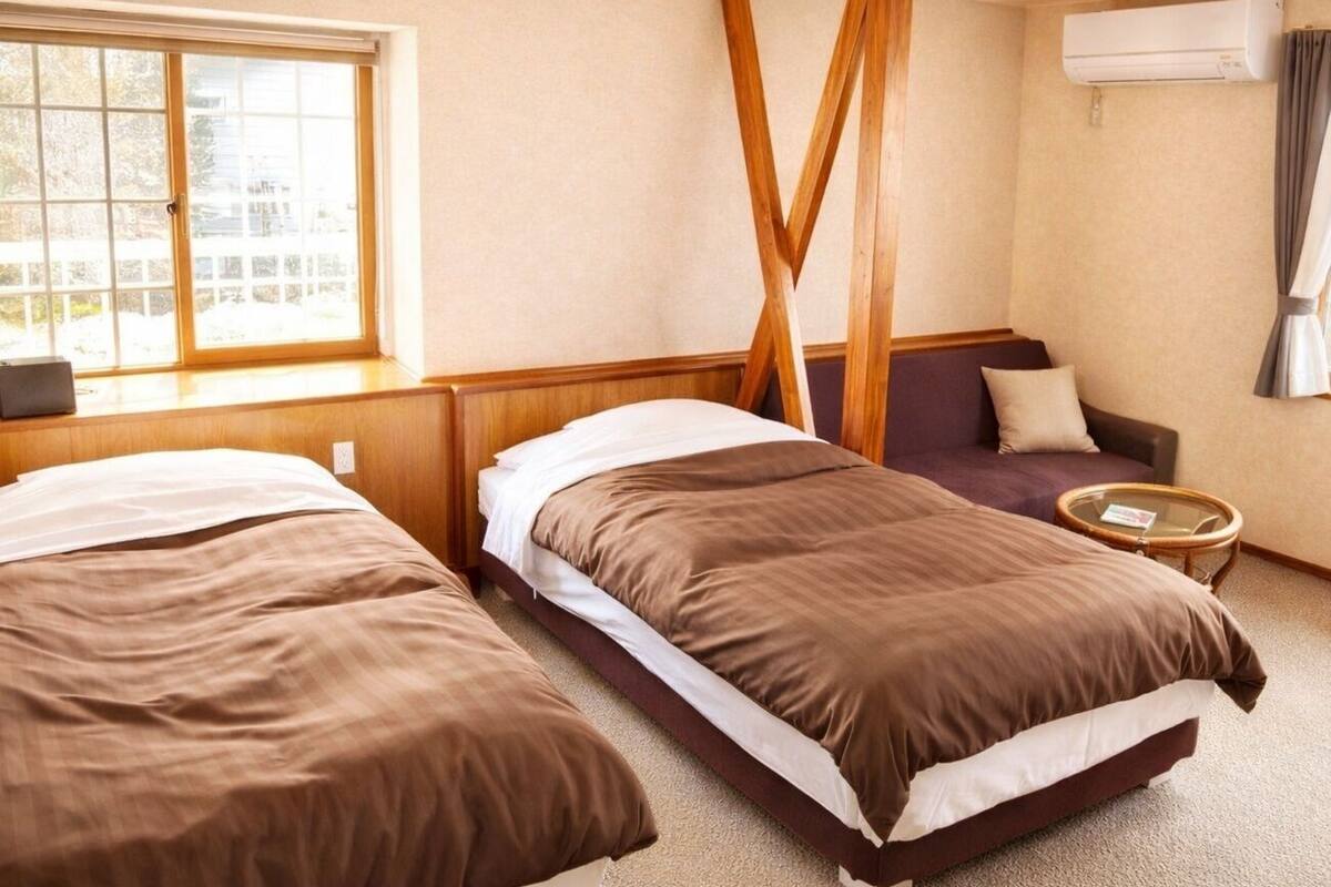 Habitación de hotel con dos camas, un sofá, una mesita redonda y un aire acondicionado.
