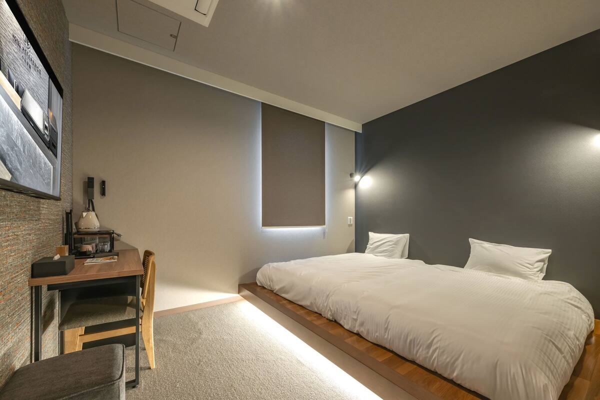 A bedroom with a bed, a desk, a chair, and a small window.