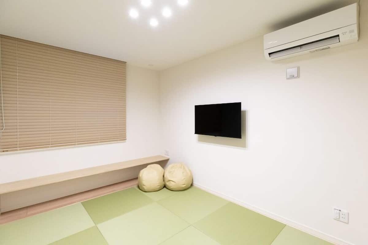 A room with a window, air conditioning unit, wall-mounted TV, tatami mats, and a low bench.