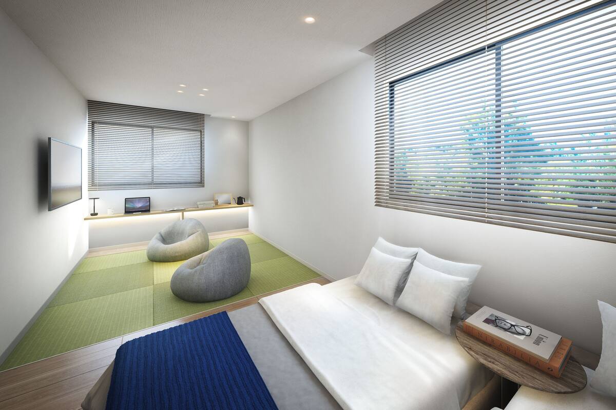 A modern bedroom with a bed, two bean bags, a desk with a computer, and a window with blinds.