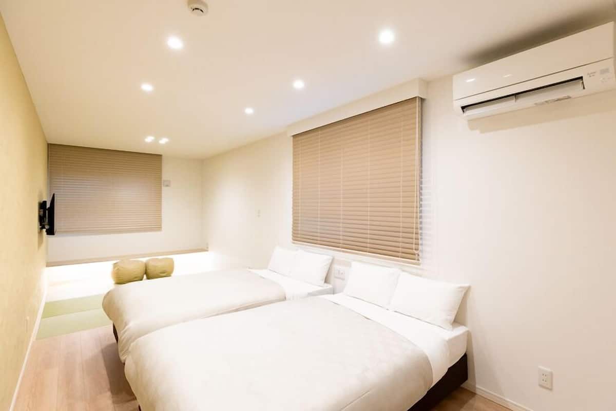 A hotel room with two beds, a wall-mounted air conditioner, and a window with blinds.