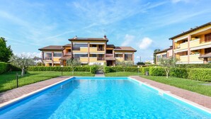 Une piscine à l’eau d’un bleu limpide, bordée d’un chemin en briques et située à côté d’un immeuble résidentiel à plusieurs étages doté de balcons.