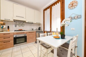 A modern kitchen with white cabinets, a dining table with chairs, and a potted plant. - MGH - Lugana Lake Apartment (Sirmione)