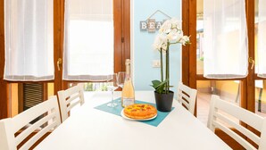 Une table à manger avec des chaises, une assiette de nourriture, une bouteille de vin et une plante en pot.