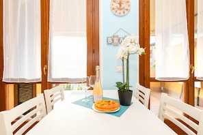 A dining table with chairs, a plate of food, a bottle of wine, and a potted plant. - MGH - Lugana Lake Apartment (Sirmione)