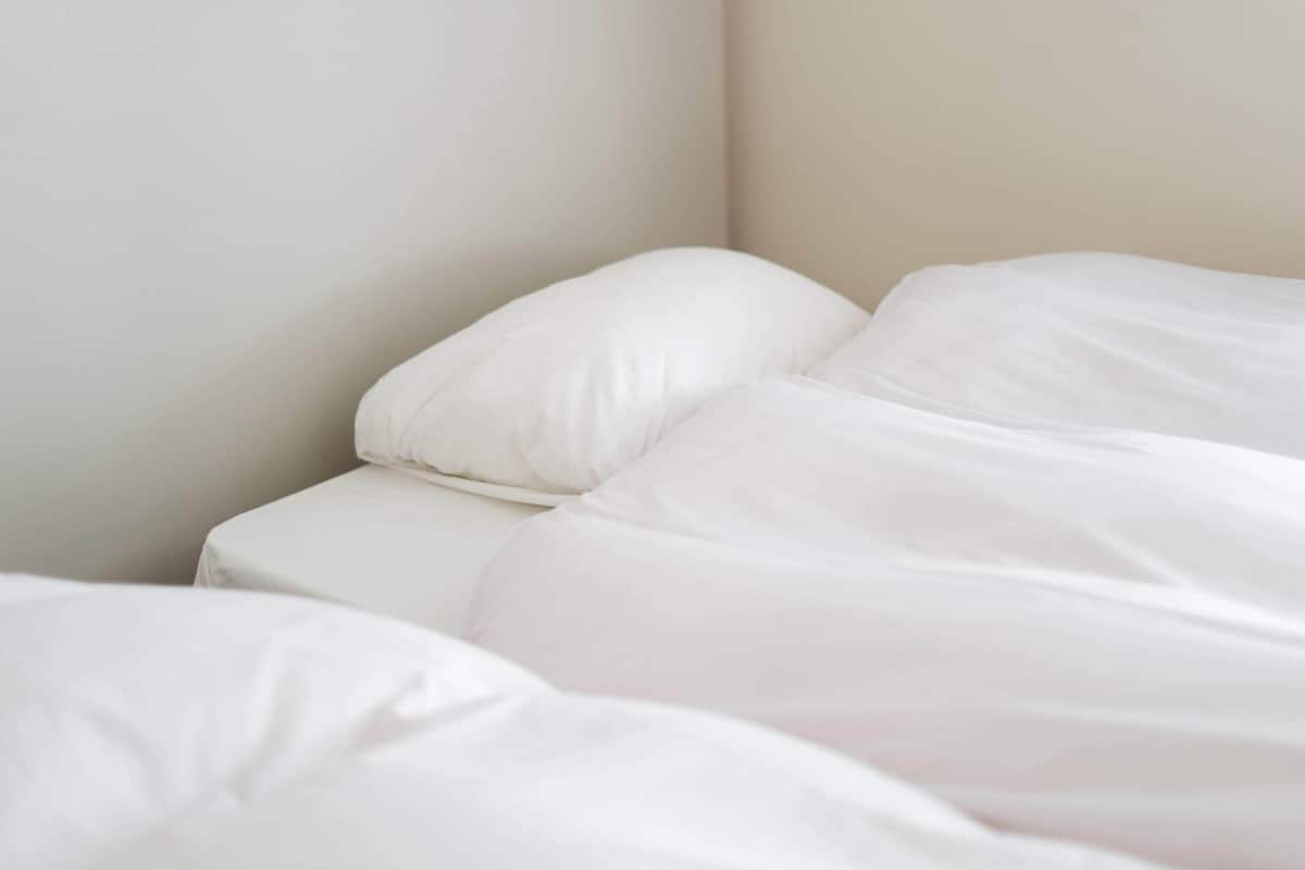 A bed with white bedding in a room with plain walls.