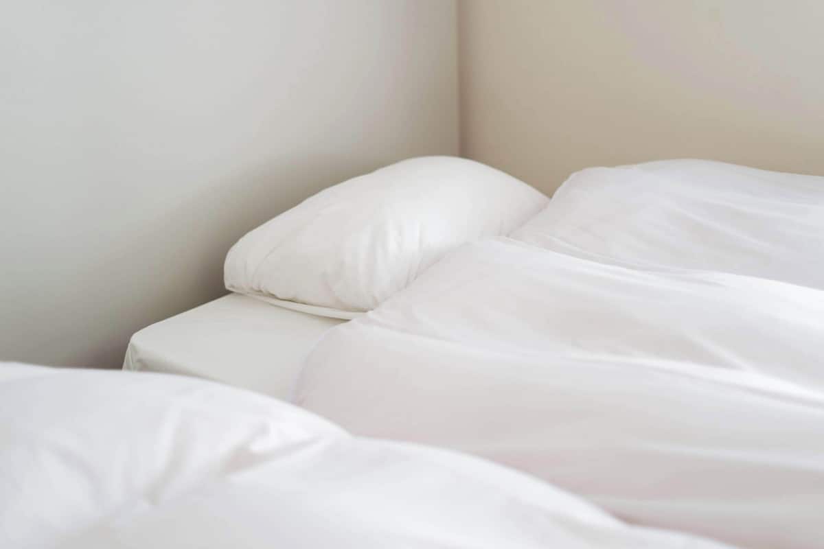 A bed with white bedding in a room with plain walls.