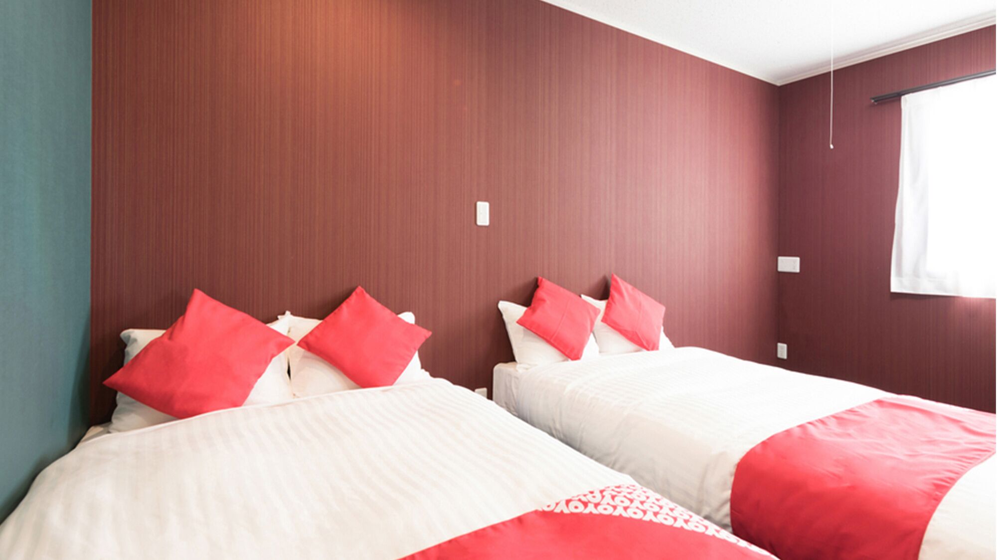 Una habitación de hotel con dos camas, ropa de cama roja y blanca, y una pared de madera.