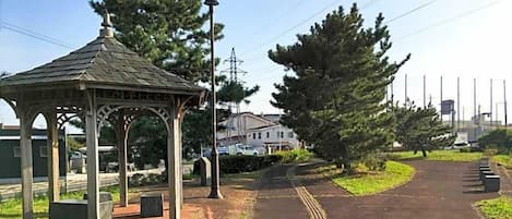 A gazebo with a roof, a paved pathway, and a row of trees.