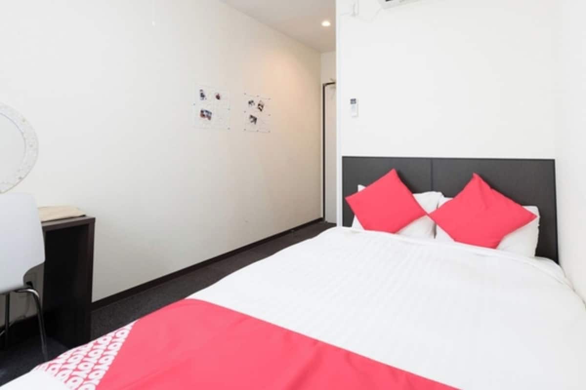 A hotel room with a bed, a nightstand, and a wall with a bulletin board.