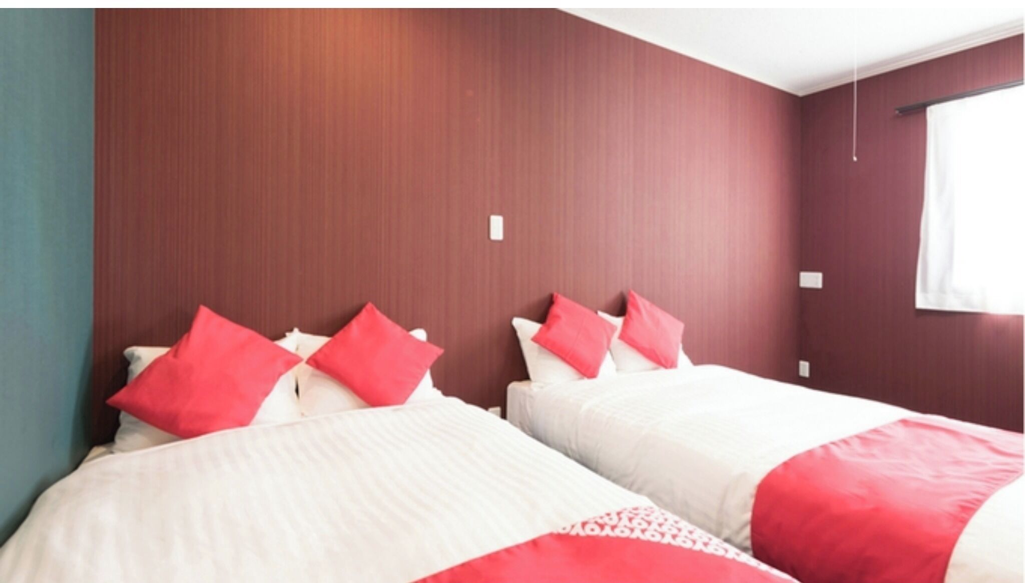 Habitación de hotel con dos camas, cada una con ropa de cama roja y blanca, y una pared de madera.