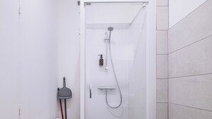 A modern shower enclosure with a glass door, a handheld showerhead, and a handheld soap dispenser.