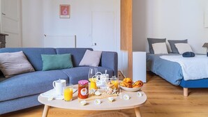 A modern room with a sofa, a bed, a breakfast table with food and drinks, and a radiator.