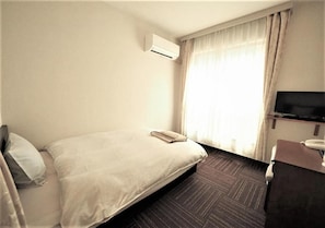 Quarto de hotel com cama, escrivaninha, cadeira, ar condicionado e televisão.