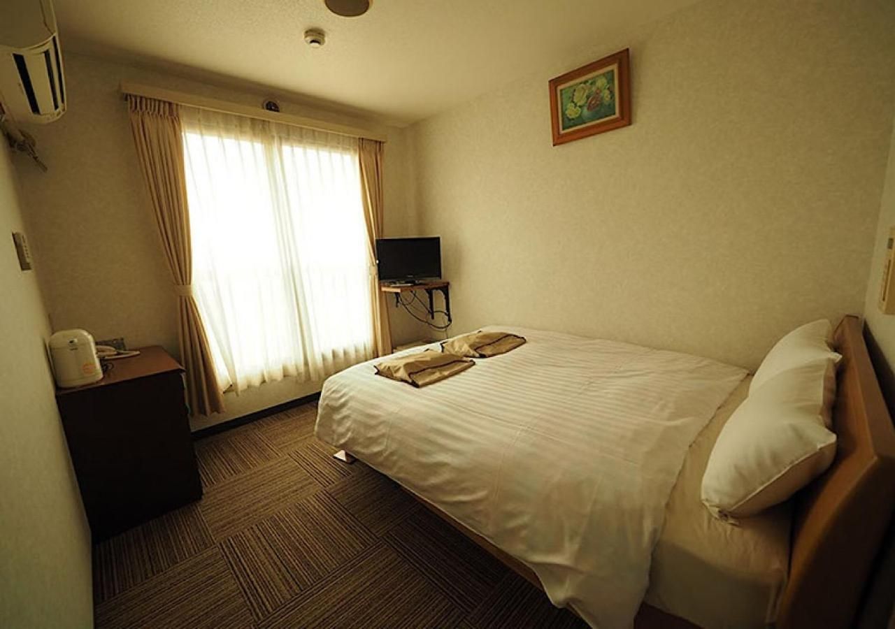 A hotel room with a bed, a desk, a television, and a window with curtains.