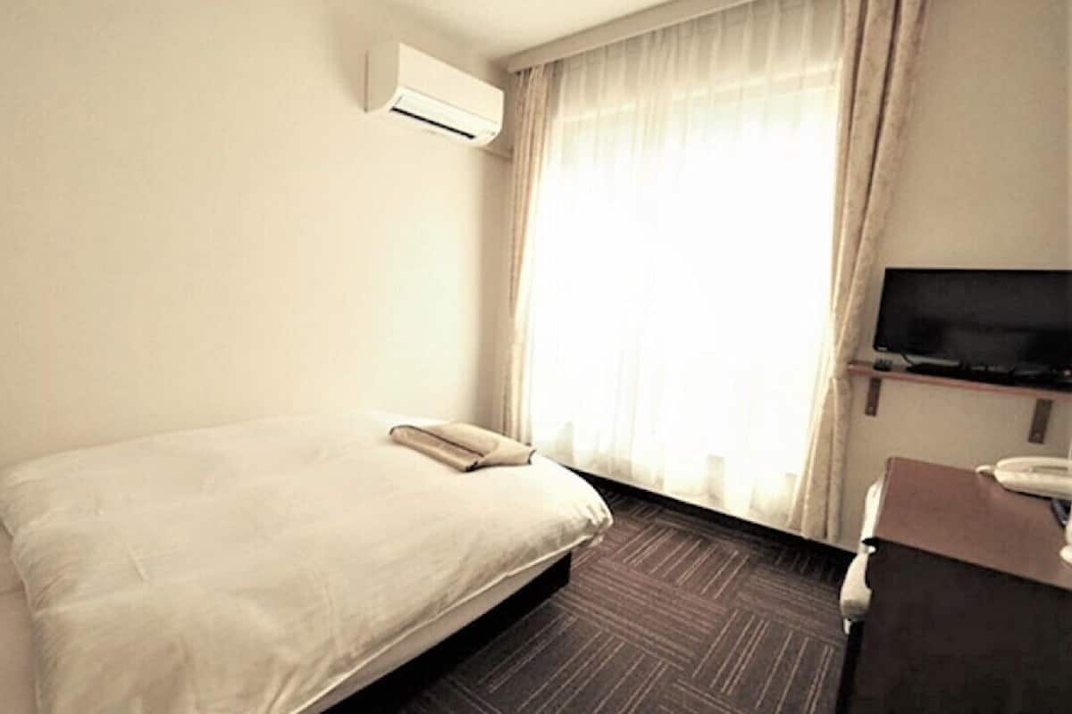 Une chambre d’hôtel avec un lit simple, un appareil de climatisation, une télévision et un bureau avec un téléphone.