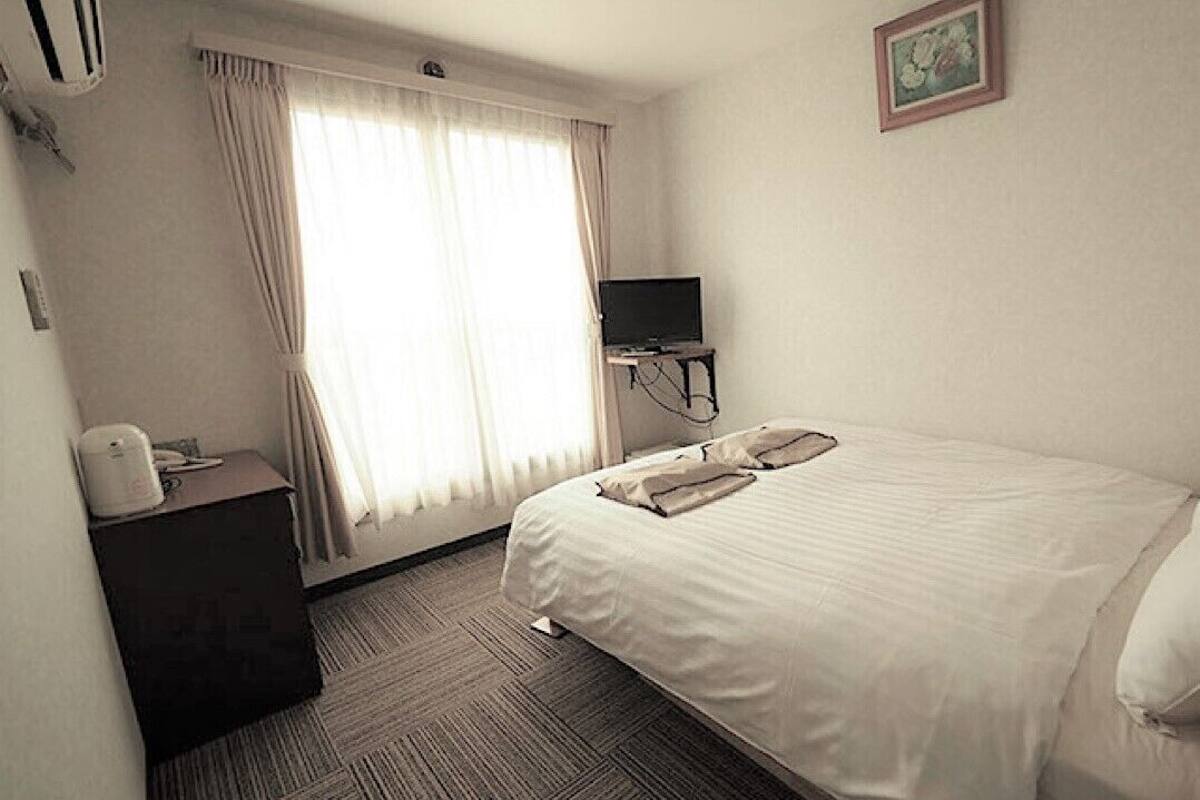Une chambre d’hôtel avec un lit, un bureau, une télévision et une fenêtre avec des rideaux.