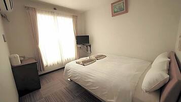A hotel room with a bed, a desk, a television, and a window with curtains.