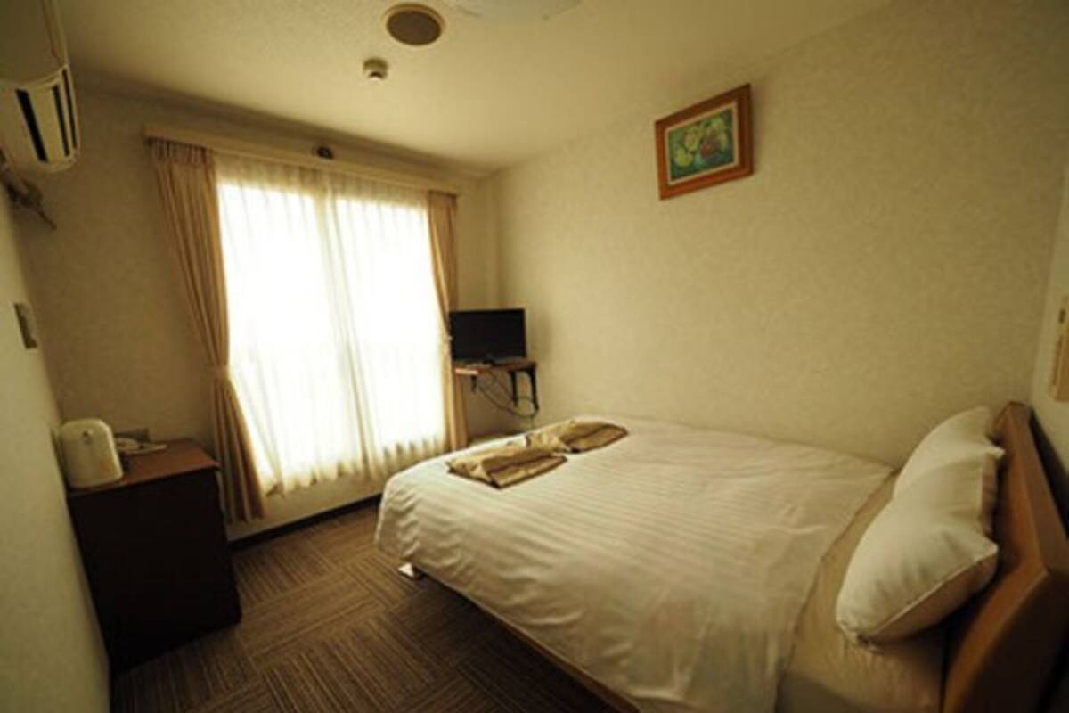 Une chambre d’hôtel avec un lit, un bureau avec un téléphone, une télévision et une fenêtre avec des rideaux.