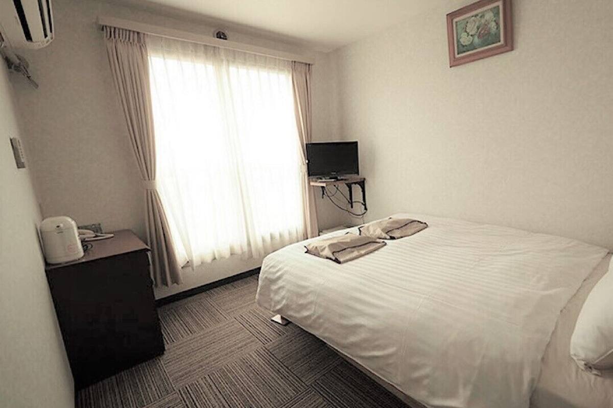 Une chambre d’hôtel comprenant un lit, un bureau avec un téléphone, un téléviseur posé sur un meuble et une fenêtre avec des rideaux.
