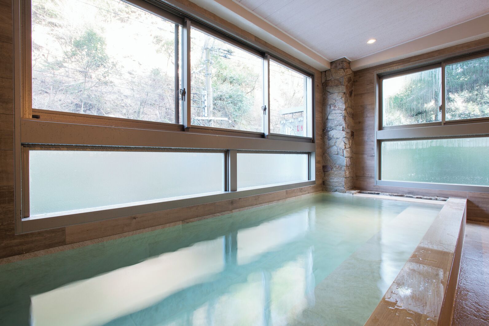 A room with a large, clear glass window, a stone wall, and a wooden floor.