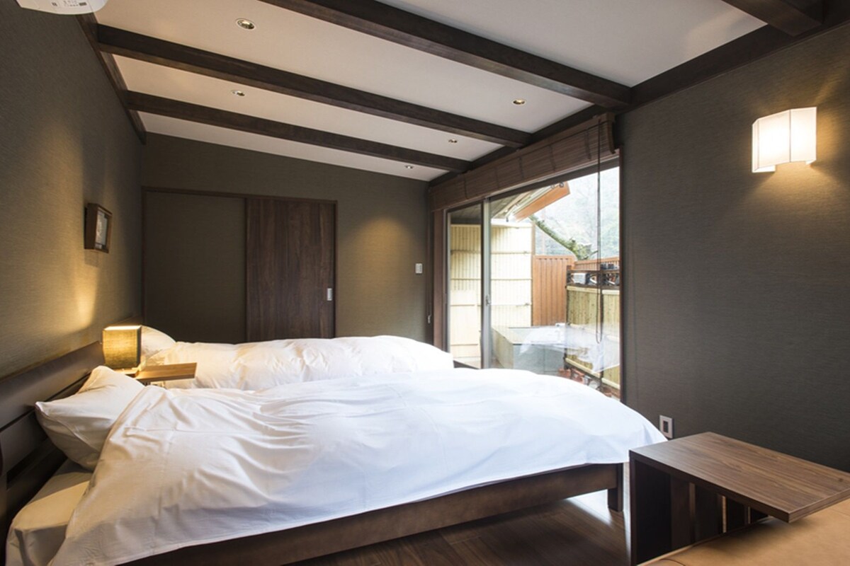 Quarto com cama, mesa de cabeceira e vista para o exterior.