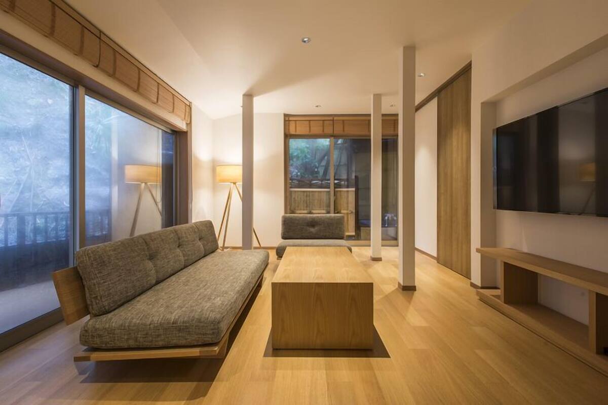 A modern living room with a sofa, a coffee table, a TV, and large windows.