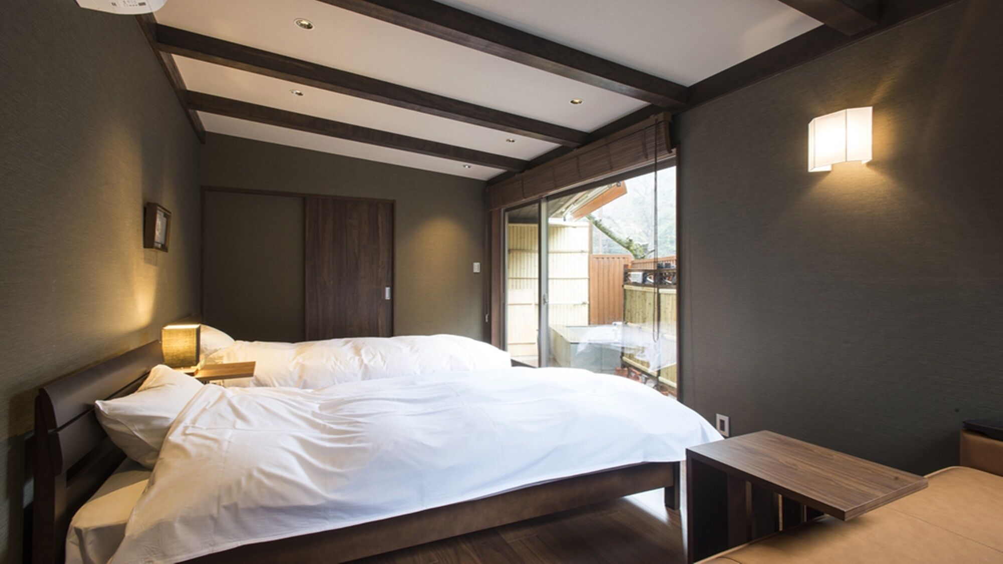 A bedroom with a bed, bedside table, and a view of the outdoors.