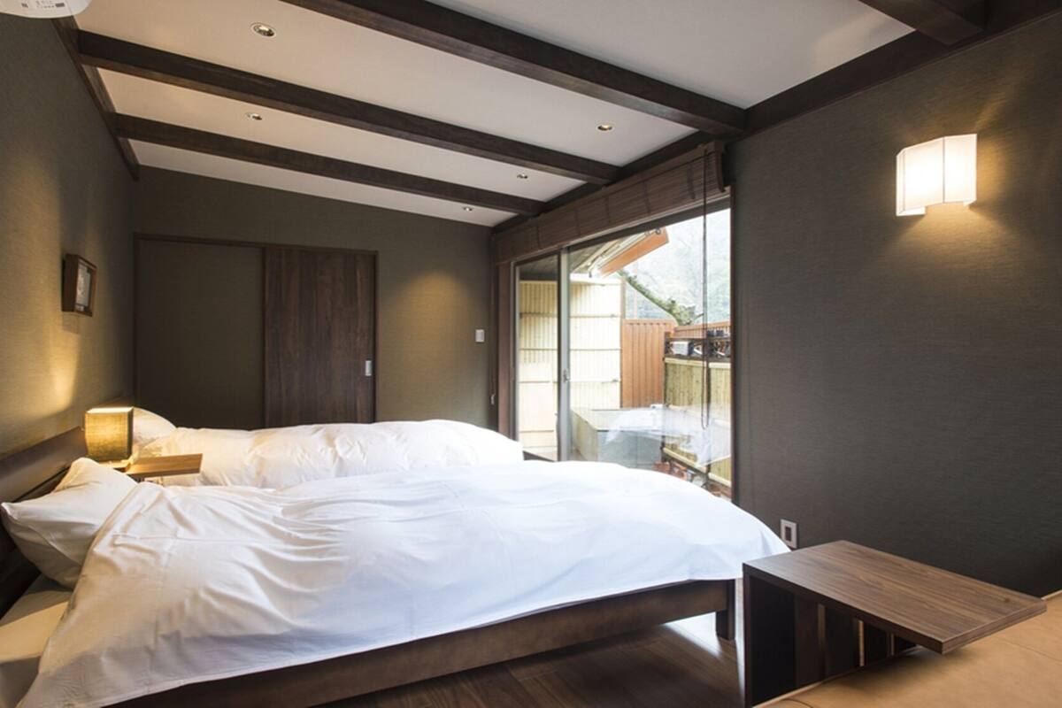 A bedroom with a bed, bedside table, and a view of the outdoors.