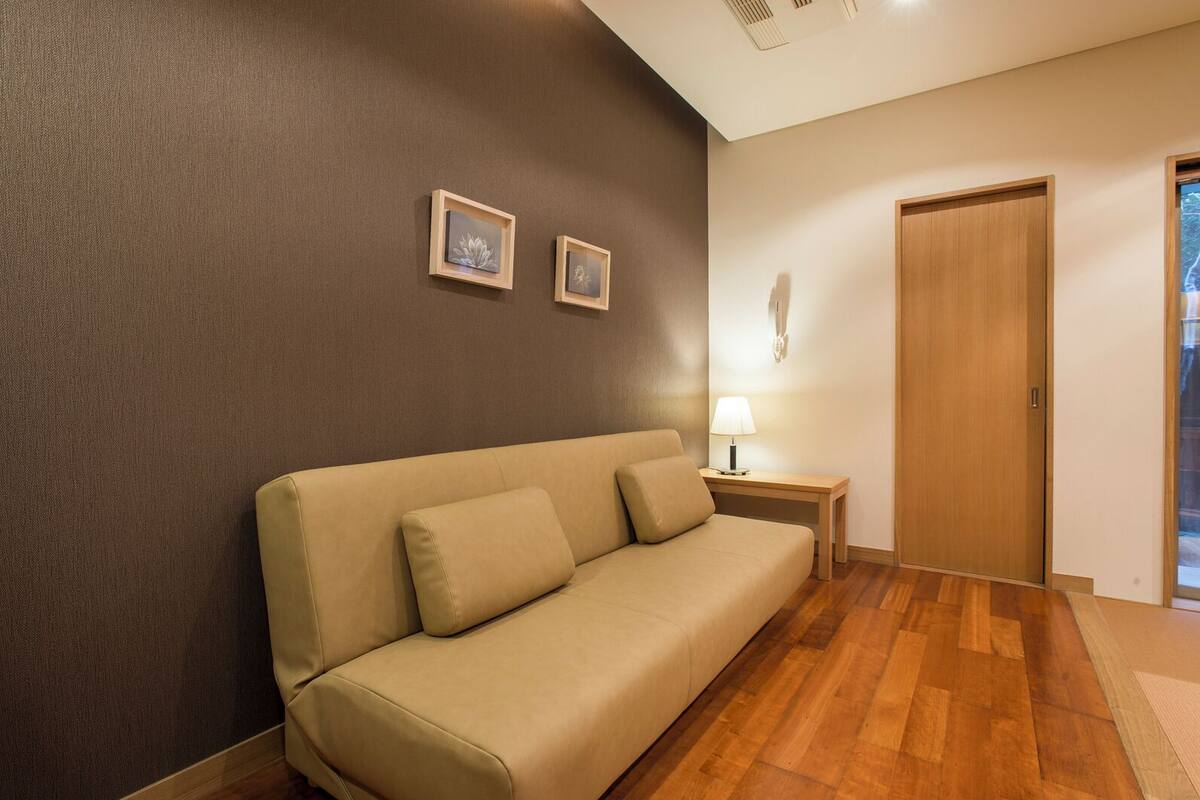 A room with a beige sofa, a wooden floor, a wall-mounted lamp, and a door.