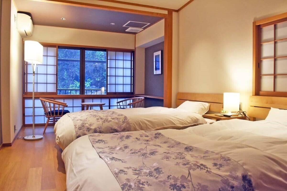 A hotel room with two beds, a window with a view, a desk, and a chair.