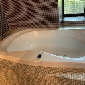 Una bañera con un tapón de drenaje en un cuarto con paredes de mosaicos.